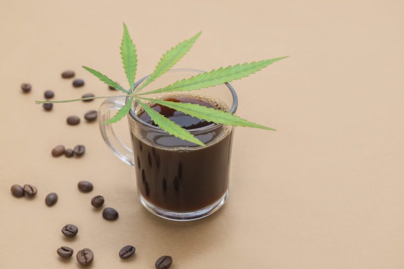 Cup of coffee with cannabis leaf and CBD products and roasted beans on neutral beige background 