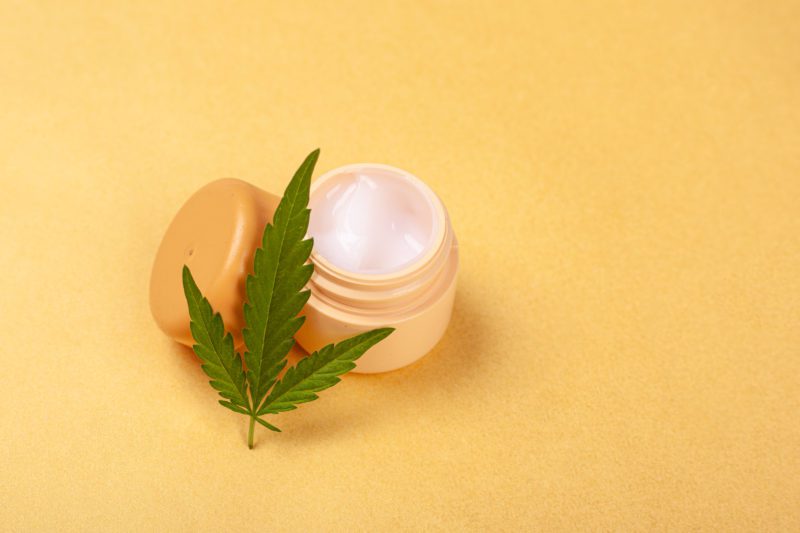 beauty, CBD skincare in Nottingham cosmetics with marijuana extract. face cream with a leaf of green cannabis on a yellow background close-up.